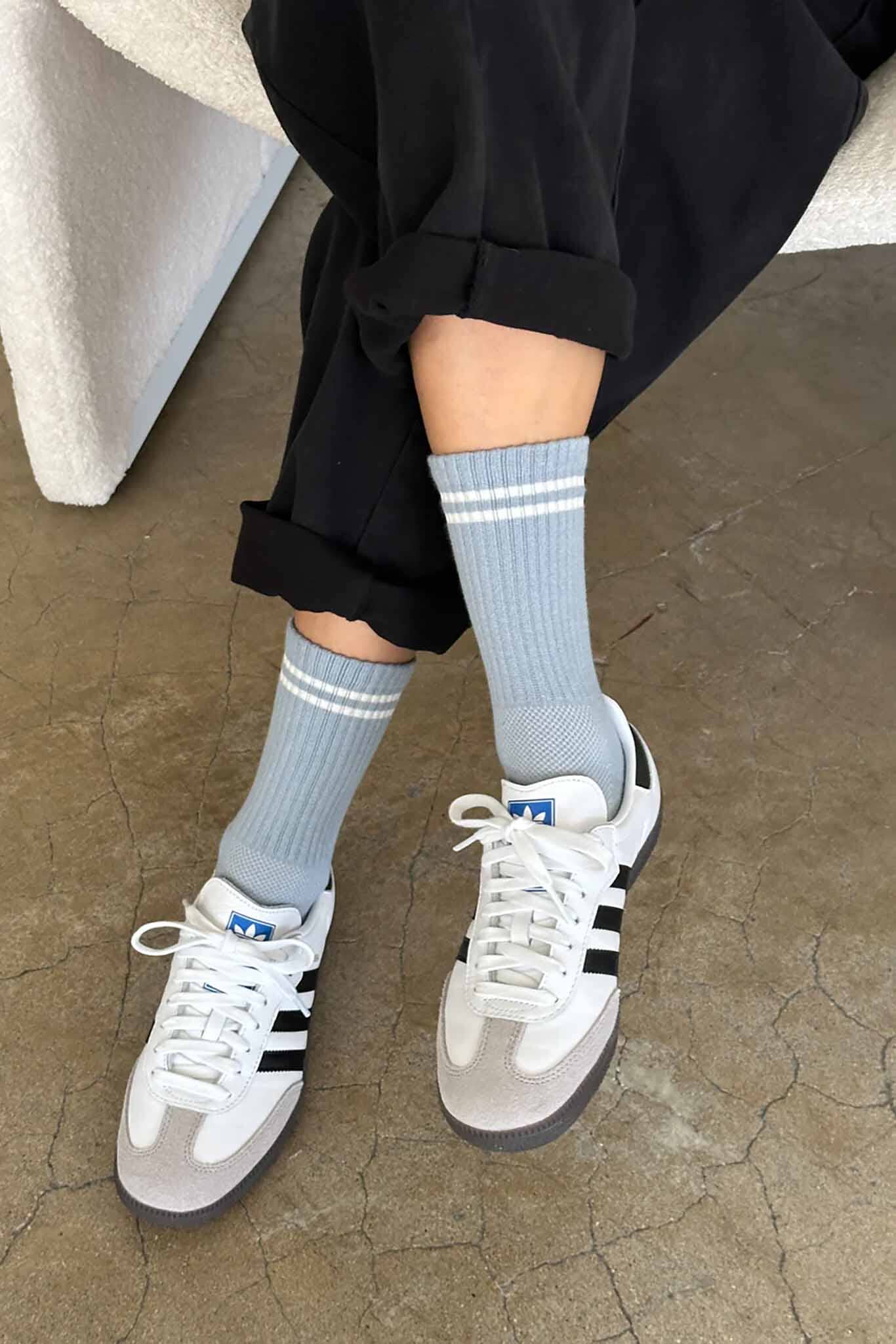 A person wearing calf-length blue grey socks with white sneakers, the socks reach mid-calf and have a striped pattern near the top.