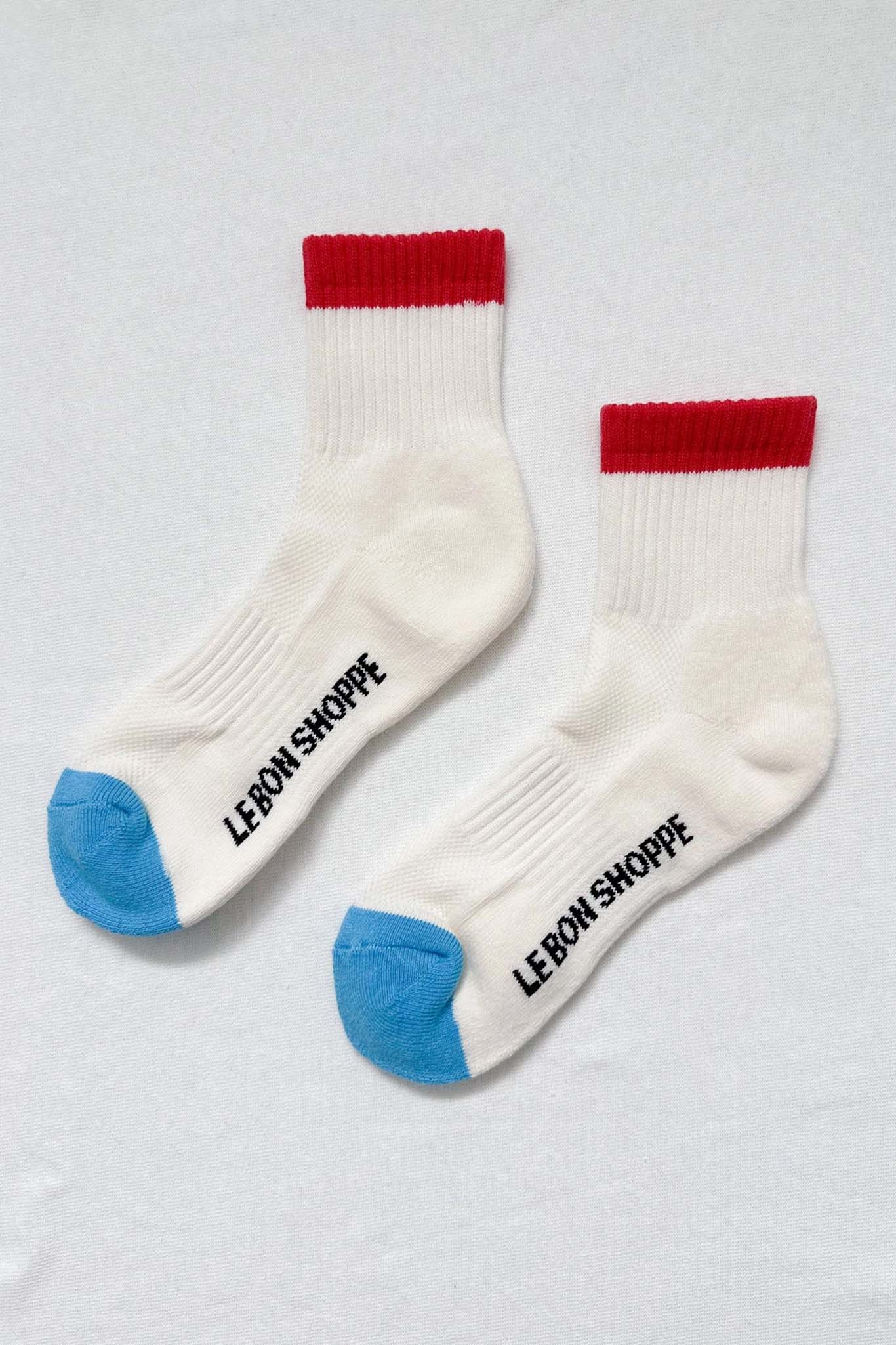 Two white socks with red tops and blue toes on a light gray background