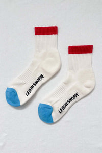 Two white socks with red tops and blue toes on a light gray background