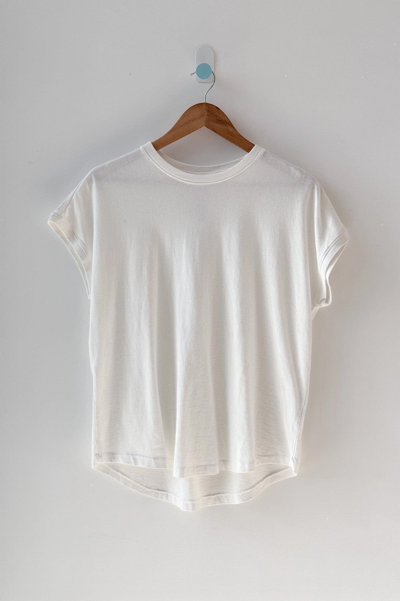 White t-shirt on a wooden hanger against a plain white background