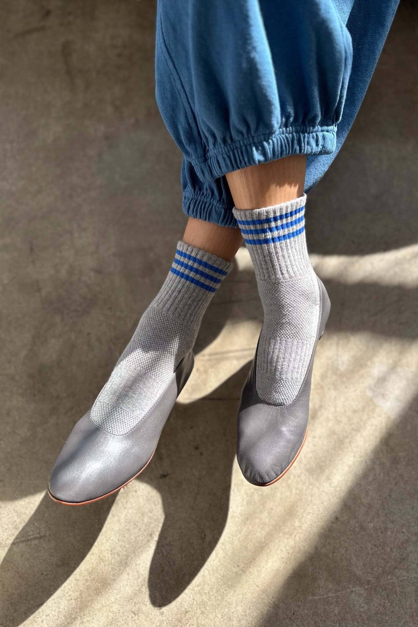 Person wearing blue pants, gray shoes, and striped socks on a concrete surface