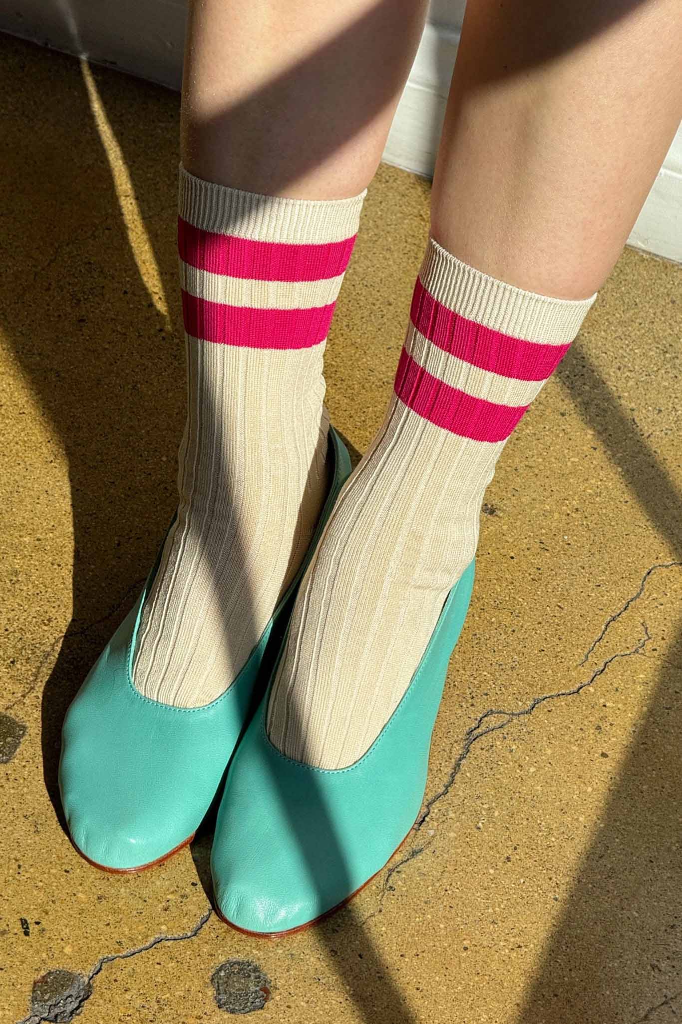Person wearing striped socks and turquoise shoes on a textured floor.
