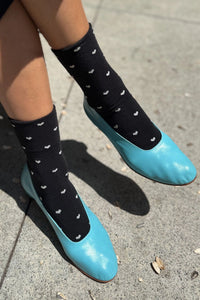 Person wearing black socks with white patterns and blue shoes on a concrete surface