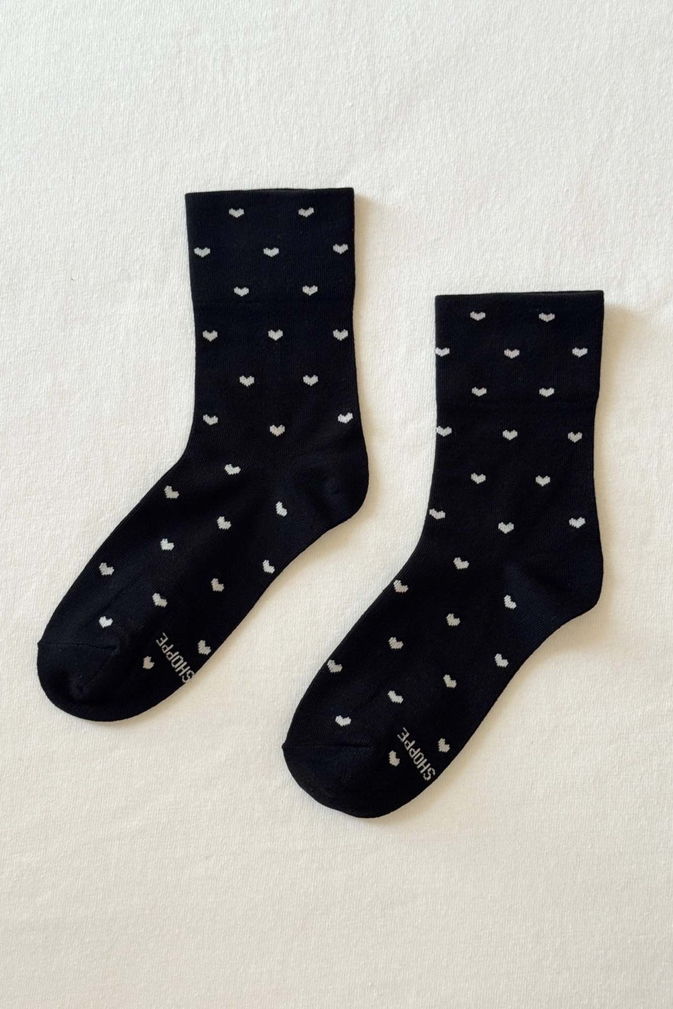 Pair of black socks with white heart patterns on a light beige background