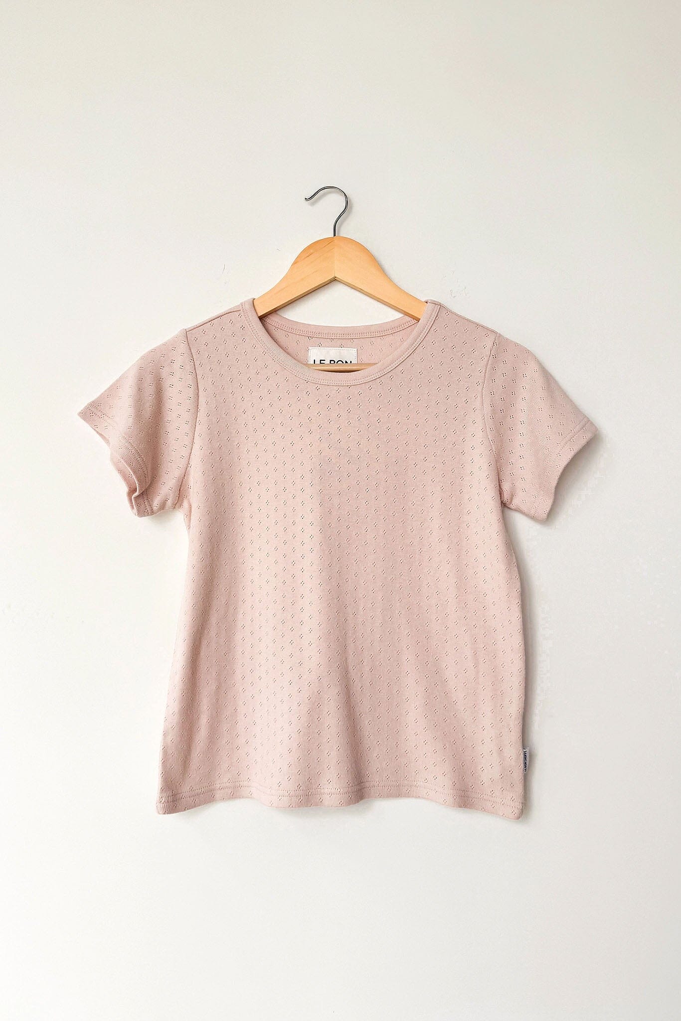Pink t-shirt on a wooden hanger against a white background