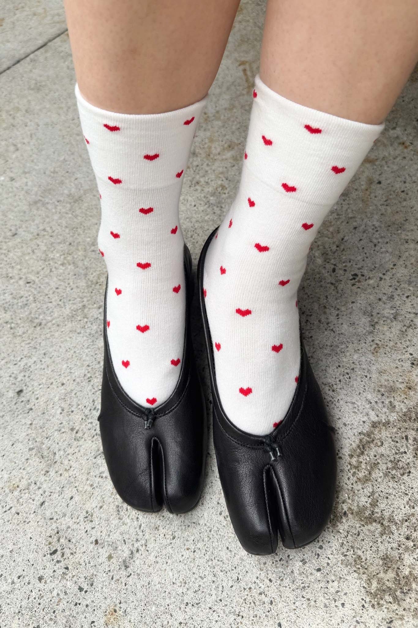 White socks with red heart patterns worn with black shoes on a concrete surface