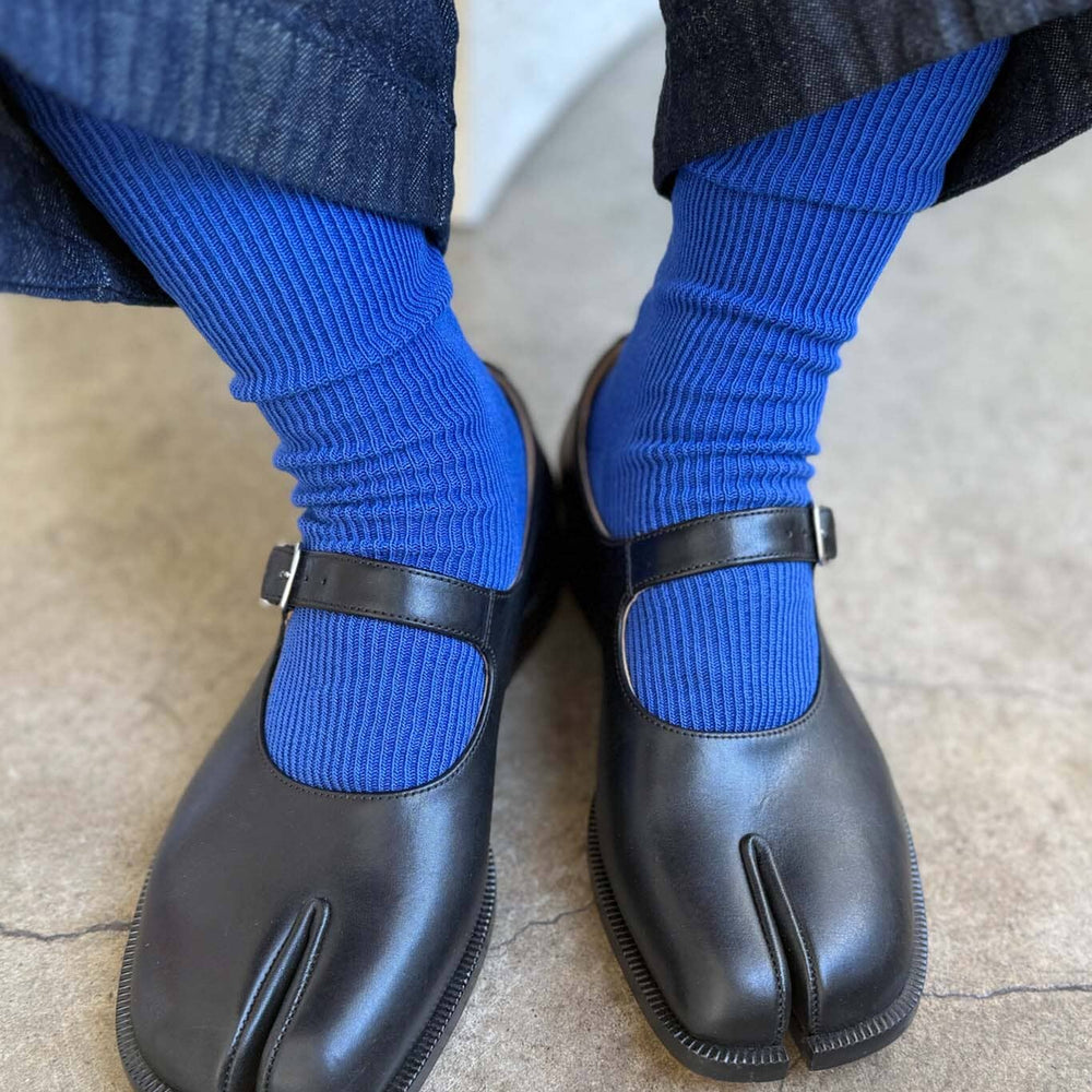 
                  
                    Black tabi shoes worn with blue socks on a light-colored floor.
                  
                