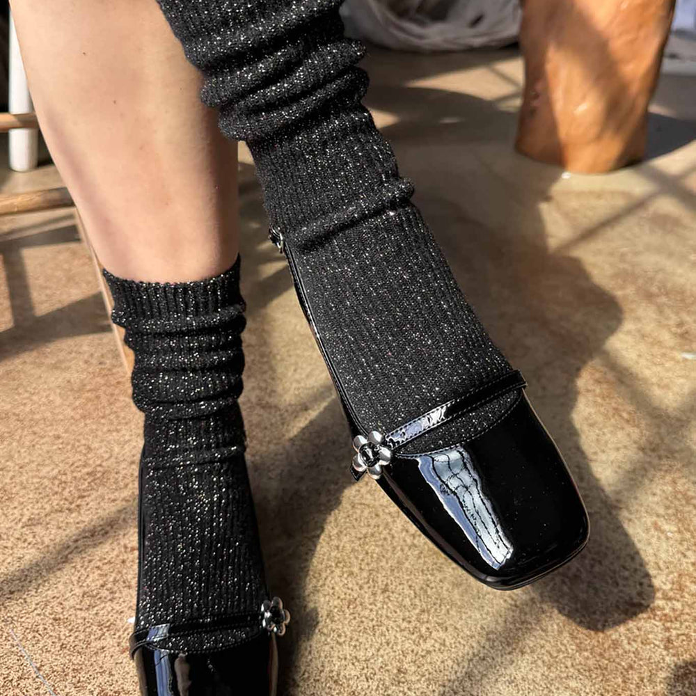 A person wearing black glitter ribbed crew socks with black mary jane shoes