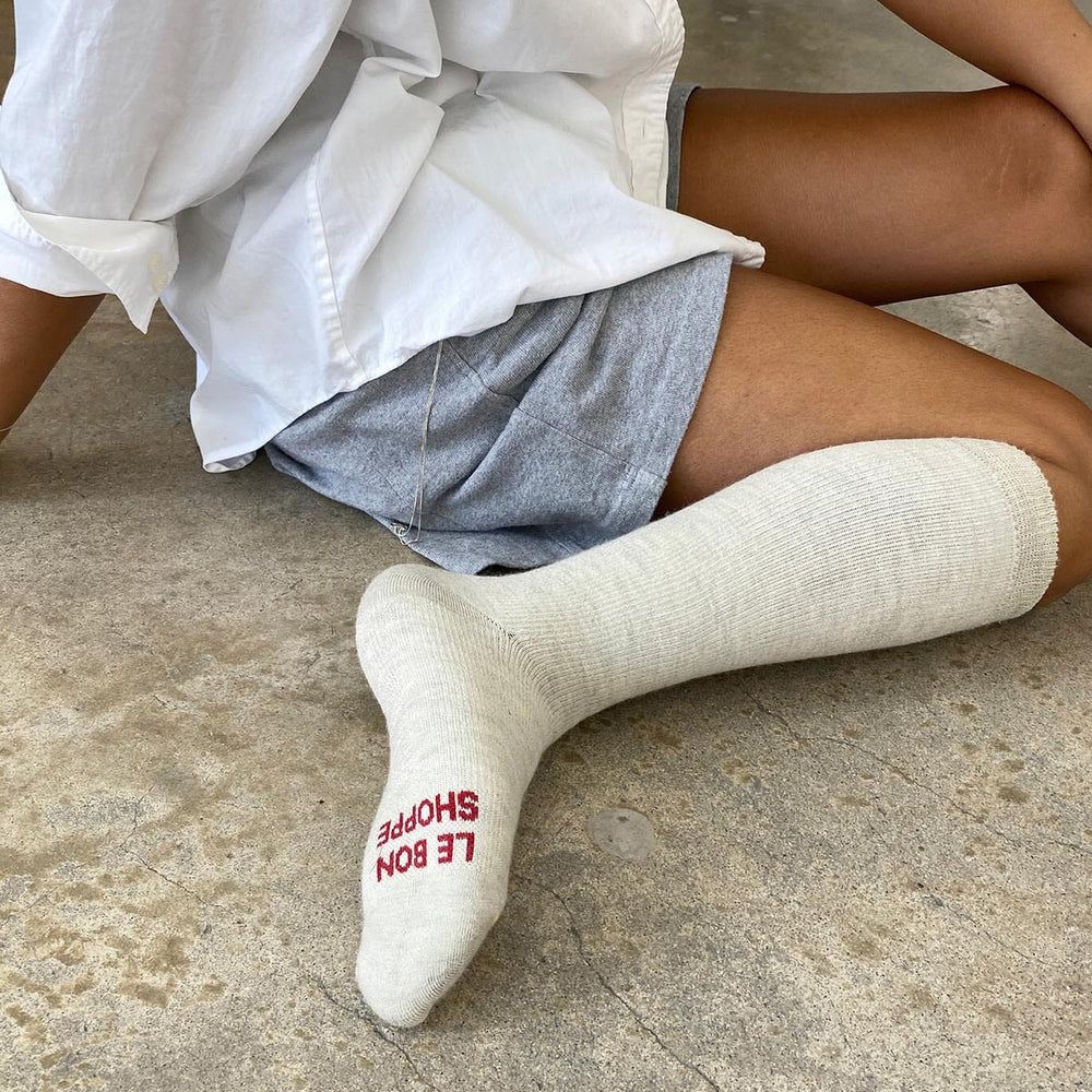 A person sitting on the floor wearing gray hiker socks with logo on the sole