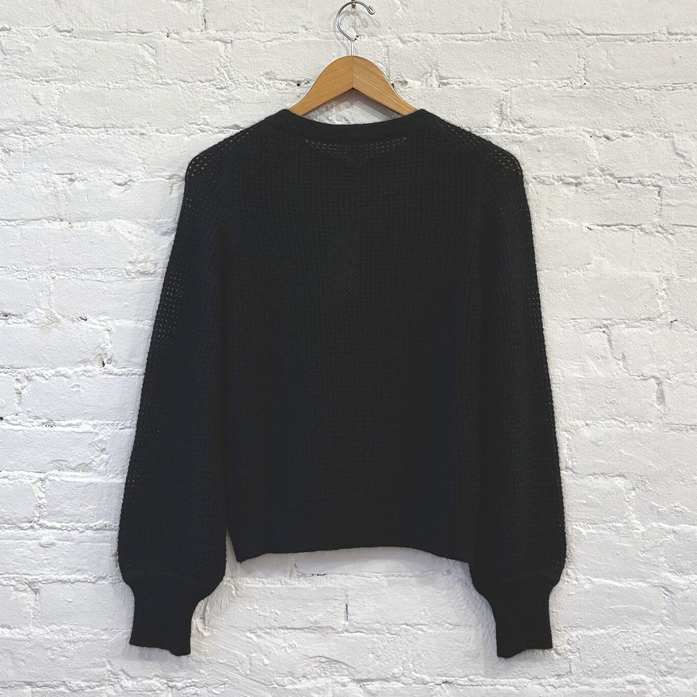 The back of a black knit cashmere sweater on a wooden hanger against a white brick wall