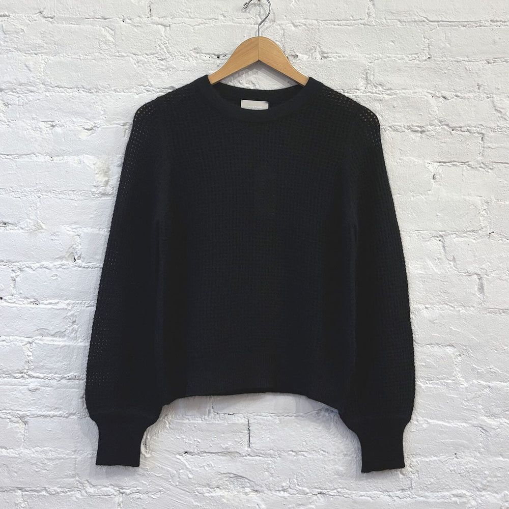 Black knit sweater on a wooden hanger against a white brick wall.