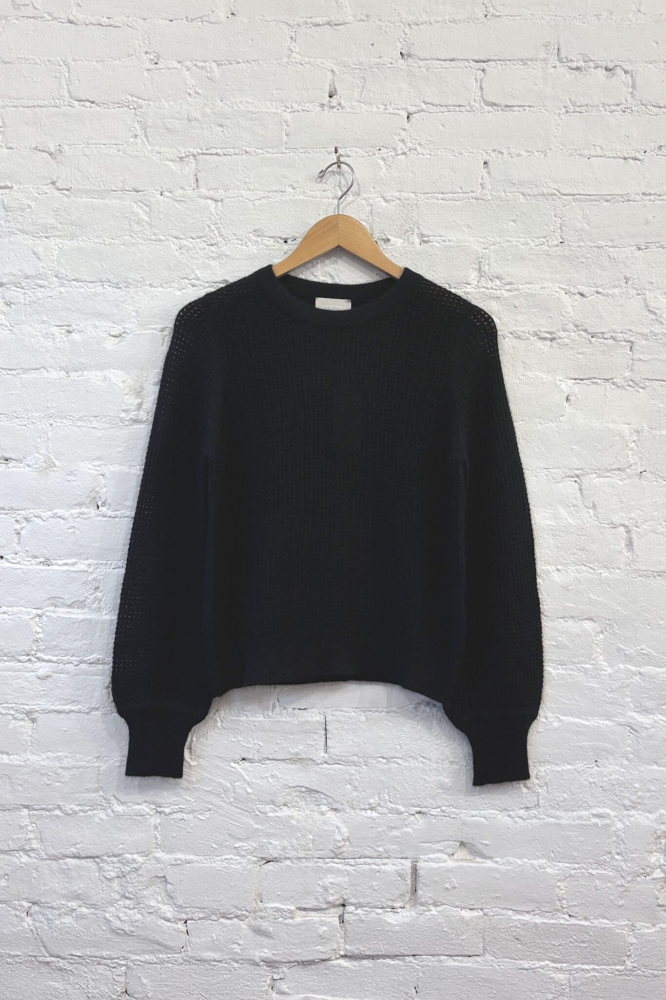 Black knit sweater on a wooden hanger against a white brick wall.