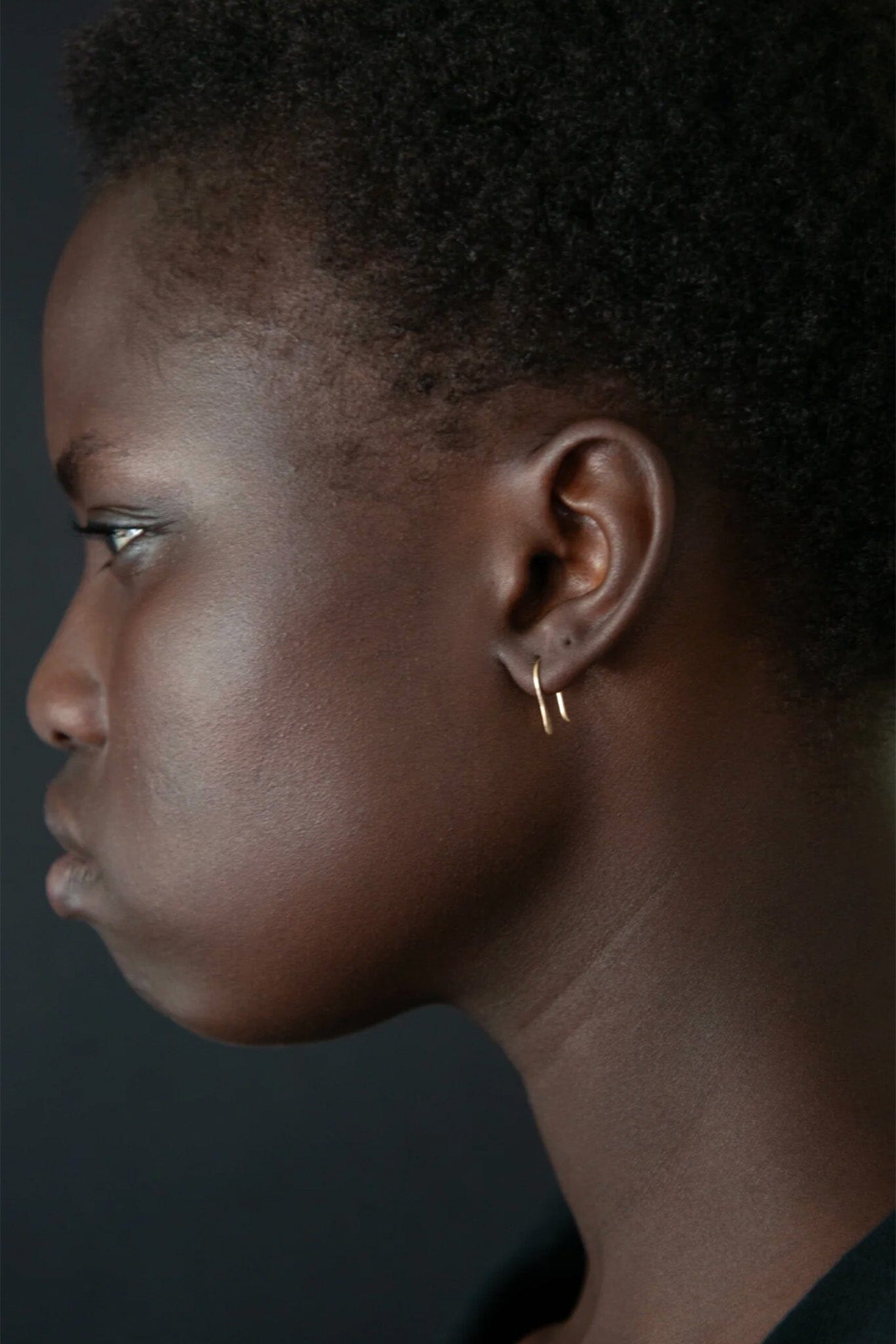 Profile of a person wearing a gold hoop earring against a dark background