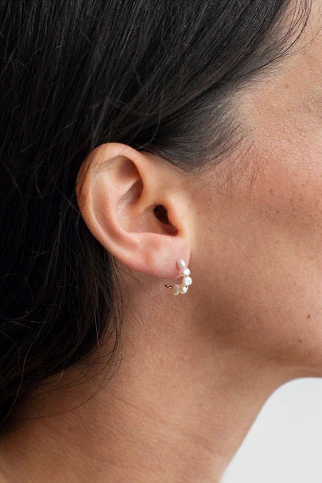 Close-up of an ear wearing a pearl earring with dark hair and a white shirt.