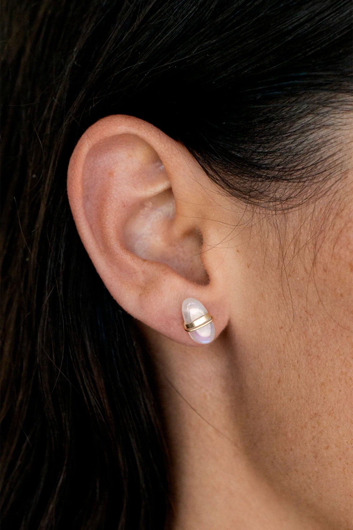 Close-up of an ear wearing a pearl earring with a dark background