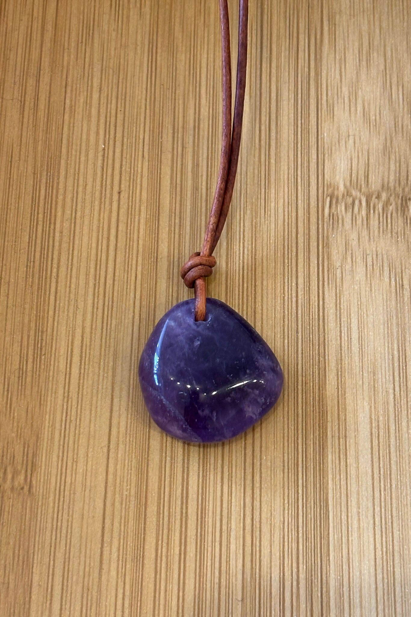 amethyst stone pendent on a brown leather cord against a wooden background