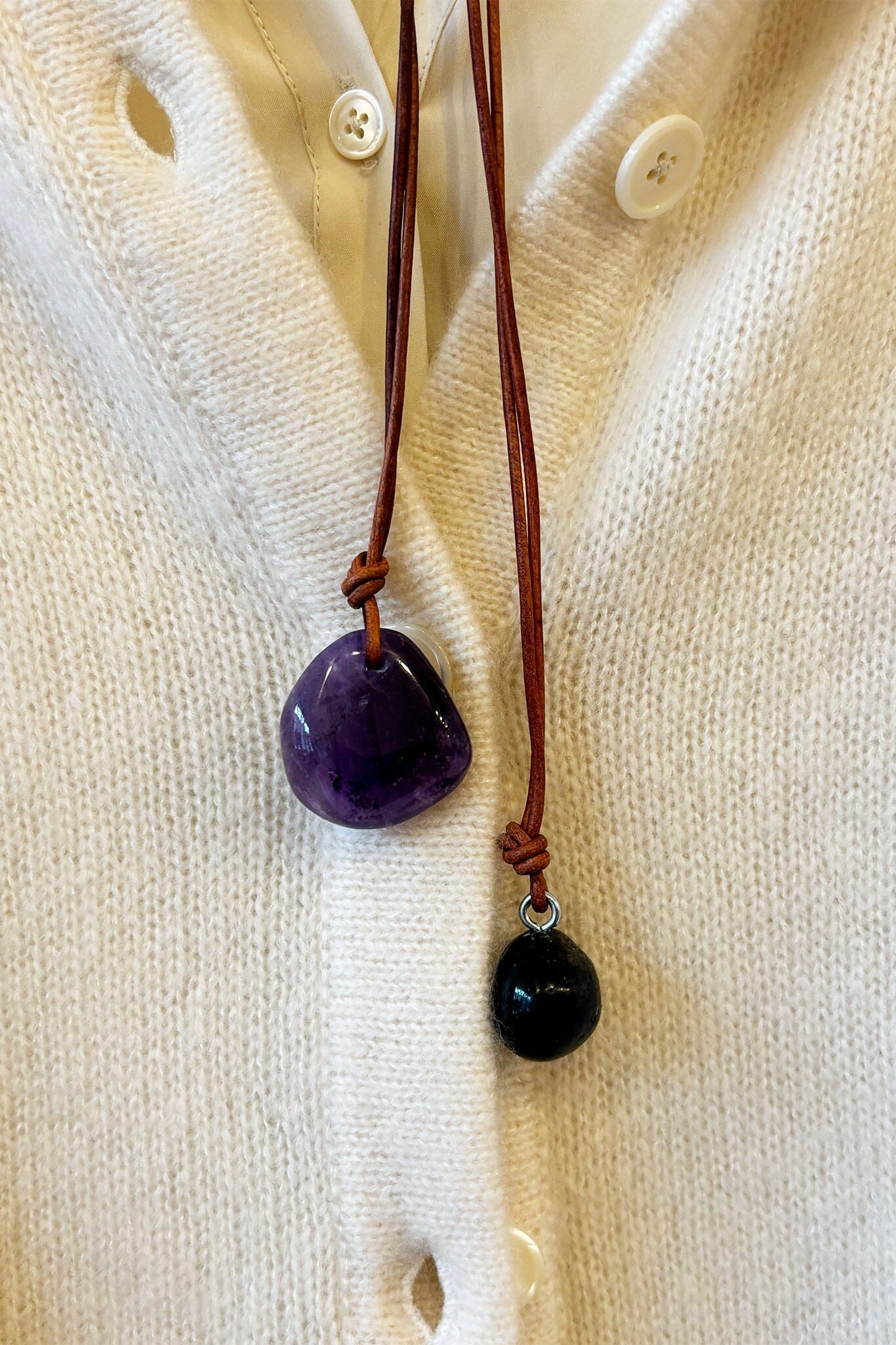 Necklace with amethyst pendant and brown cord on a white shirt