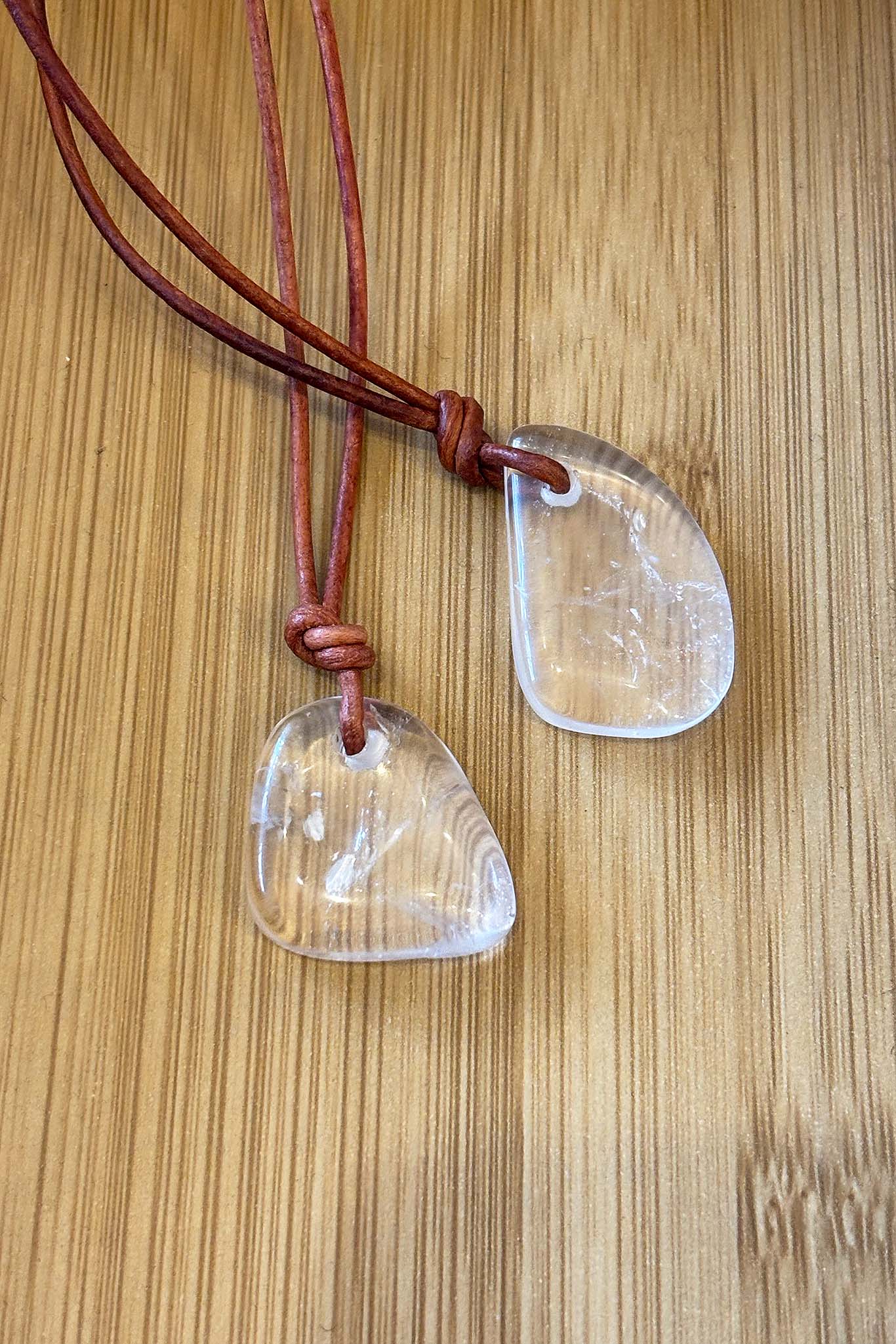 Two clear stone pendants on a brown leather cord against a wooden background