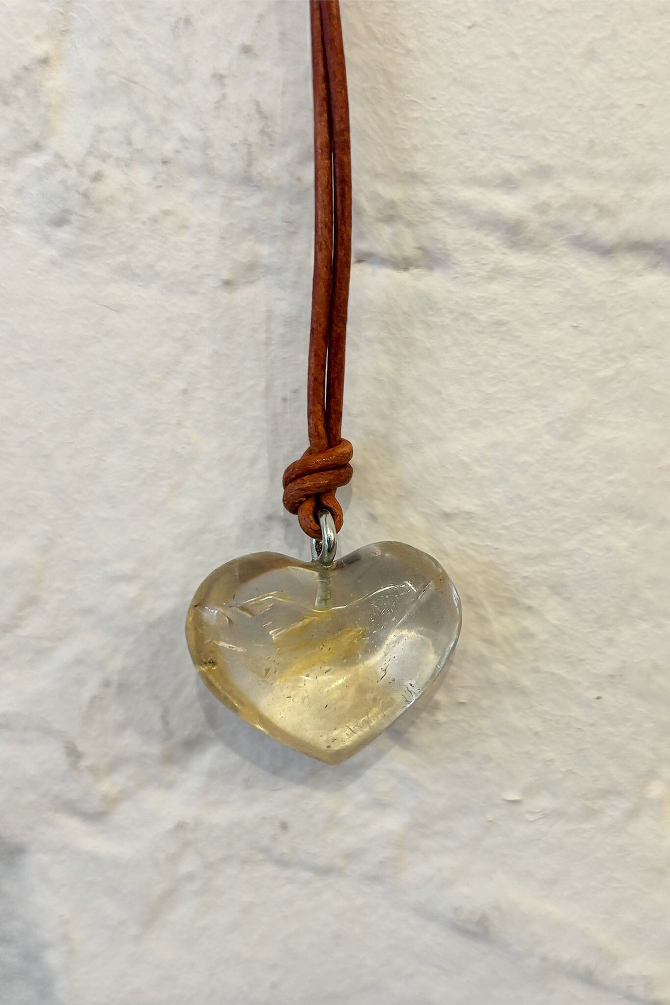 Heart-shaped pendant on a brown cord against a marble background