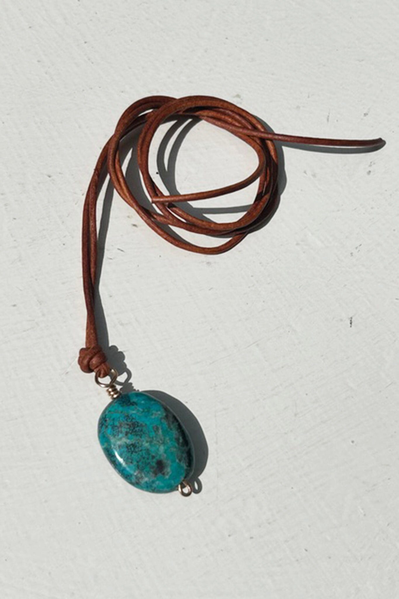 Turquoise pendant on a brown leather cord against a white background