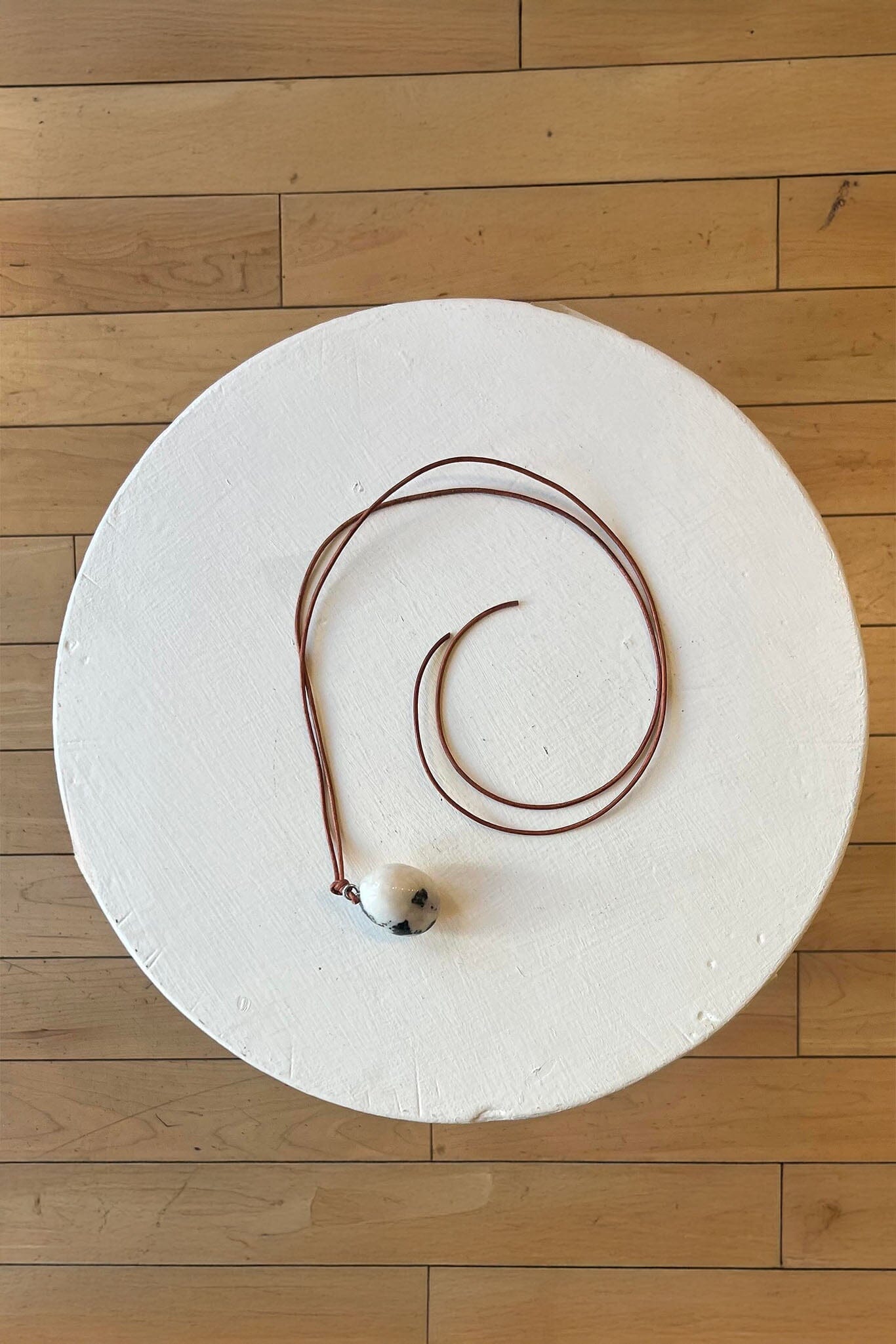 Necklace with a zebra marble pendant on a white round platform against a wooden floor background