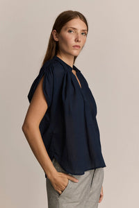 Woman wearing a lightweight, short sleeve navy blue top with sleeve gathering detail on a beige background