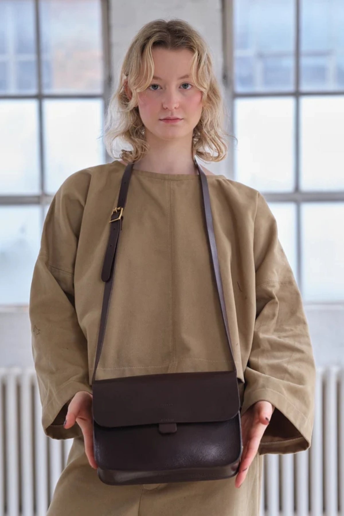 Model holding the dark brown leather Kate Sheridan Date Midi Tab Bag, showing its mid-size proportions.