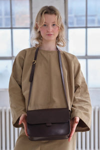 Model holding the dark brown leather Kate Sheridan Date Midi Tab Bag, showing its mid-size proportions.