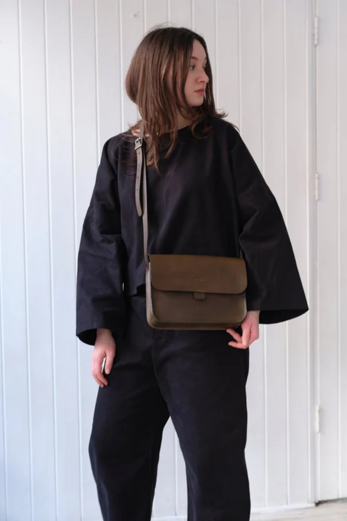 Model wearing the leather Kate Sheridan Olive Midi Tab Bag as a crossbody over a black outfit.