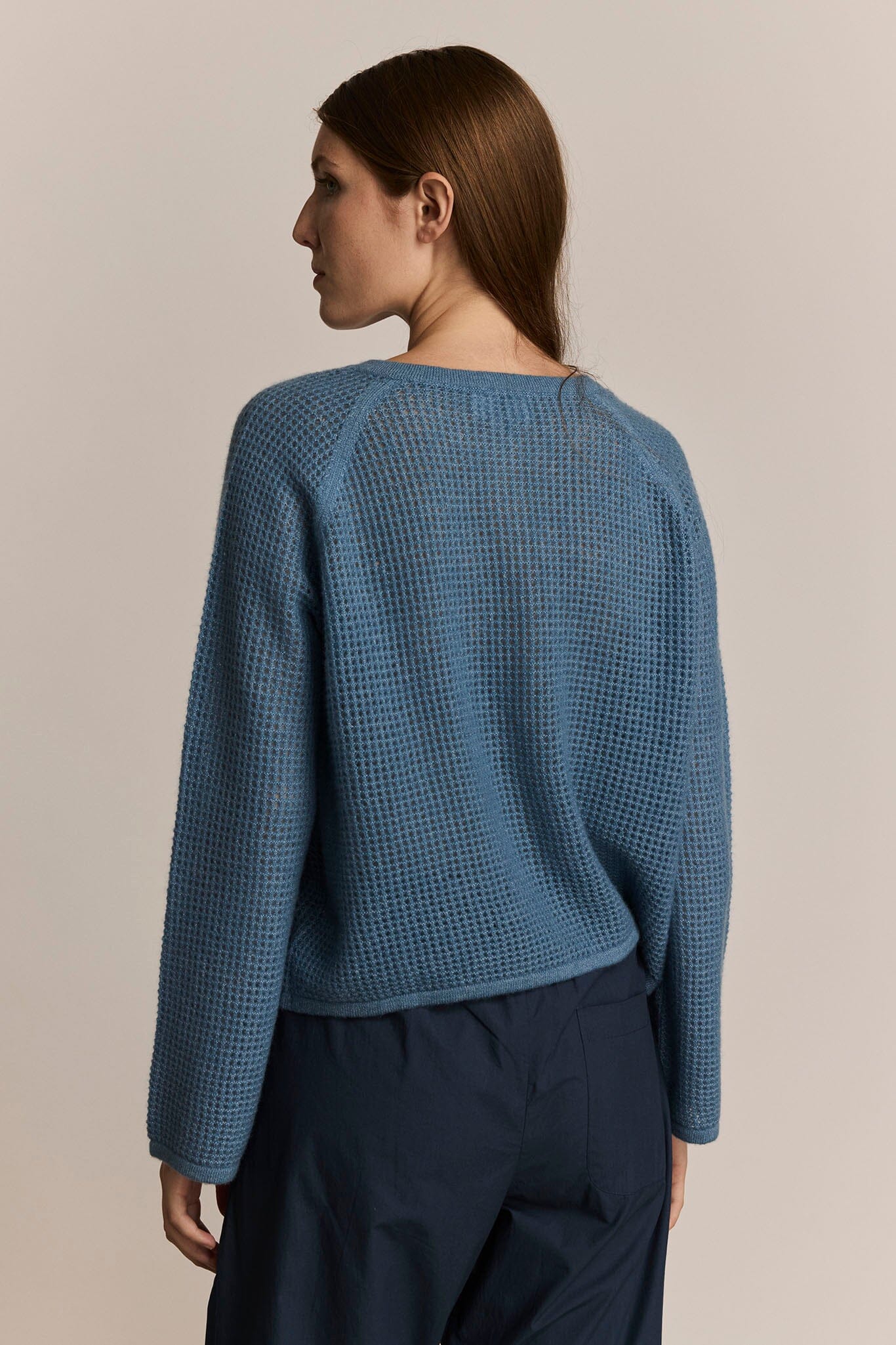 Woman wearing a blue knit cashmere sweater and dark pants against a beige background