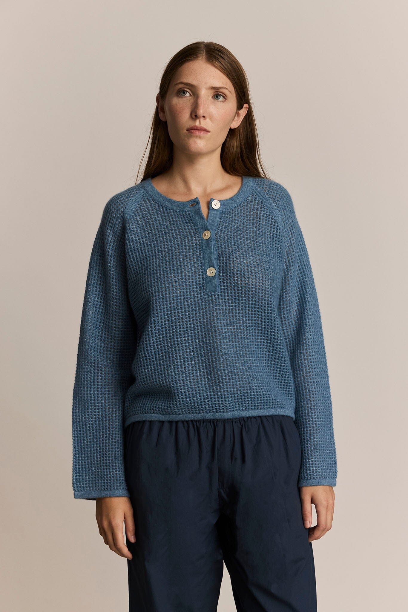 Woman wearing a blue knit henley sweater with buttons on a beige background