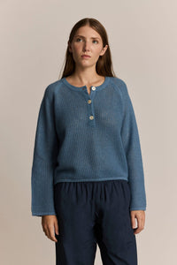 Woman wearing a blue knit henley sweater with buttons on a beige background