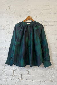Green patterned long sleeve shirt on a wooden hanger against a white brick wall.
