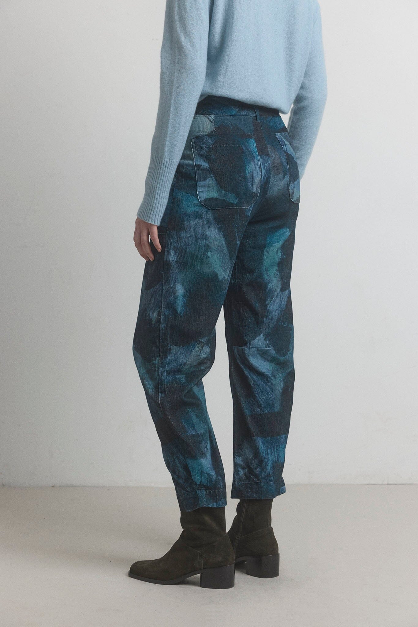 Person wearing blue tie-dye pants and black shoes on a white background