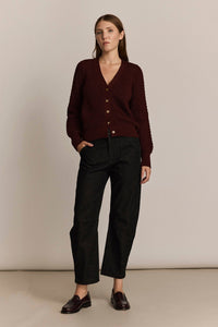 Woman wearing a burgundy cardigan and black pants against a beige background