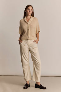 Woman wearing a beige short sleeve cardigan and the M.Patmos natural denim Anable pants against a plain background