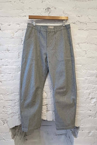 Striped pants hanging on a wooden hanger against a white brick wall.