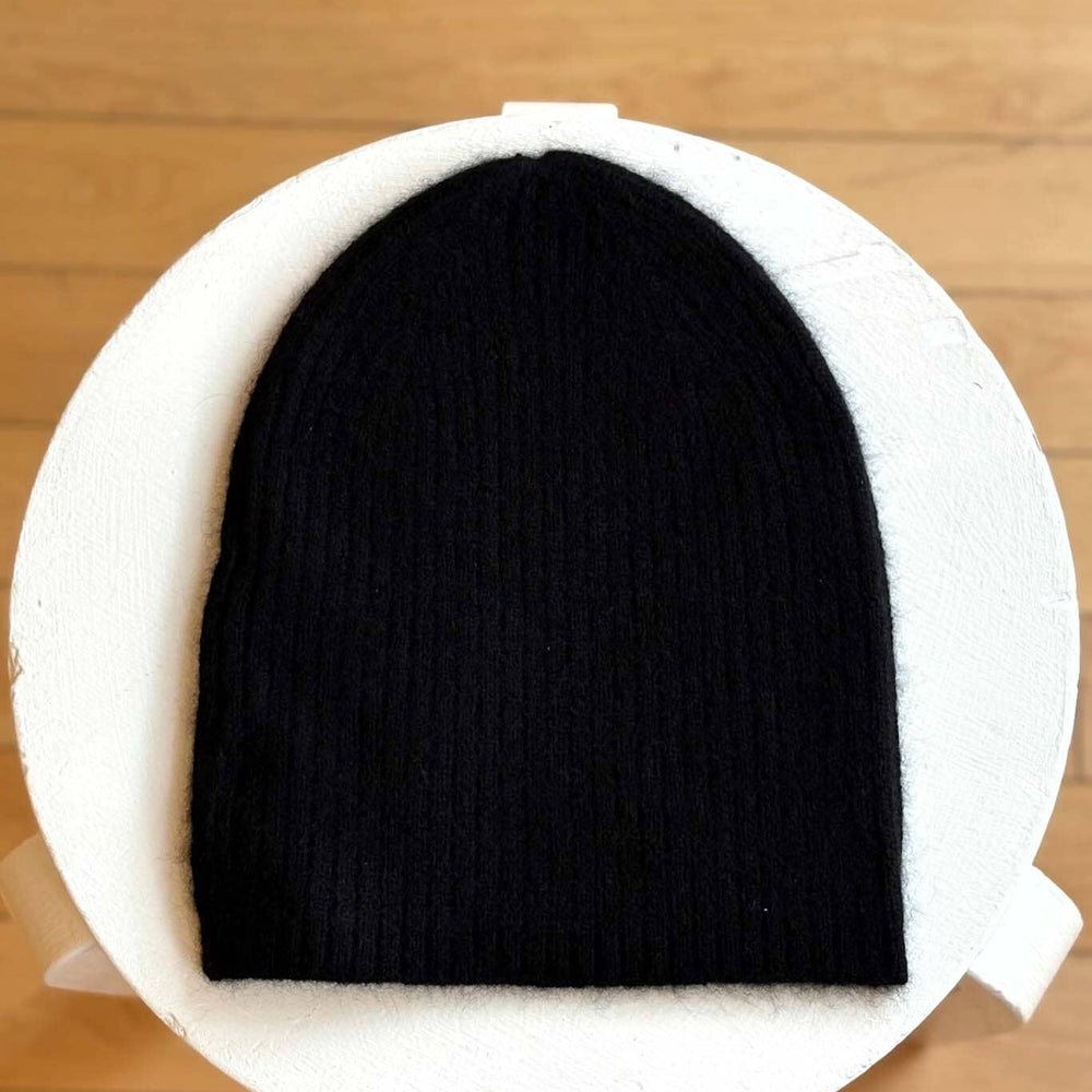 Black beanie on a white circular cushion with a wooden floor background