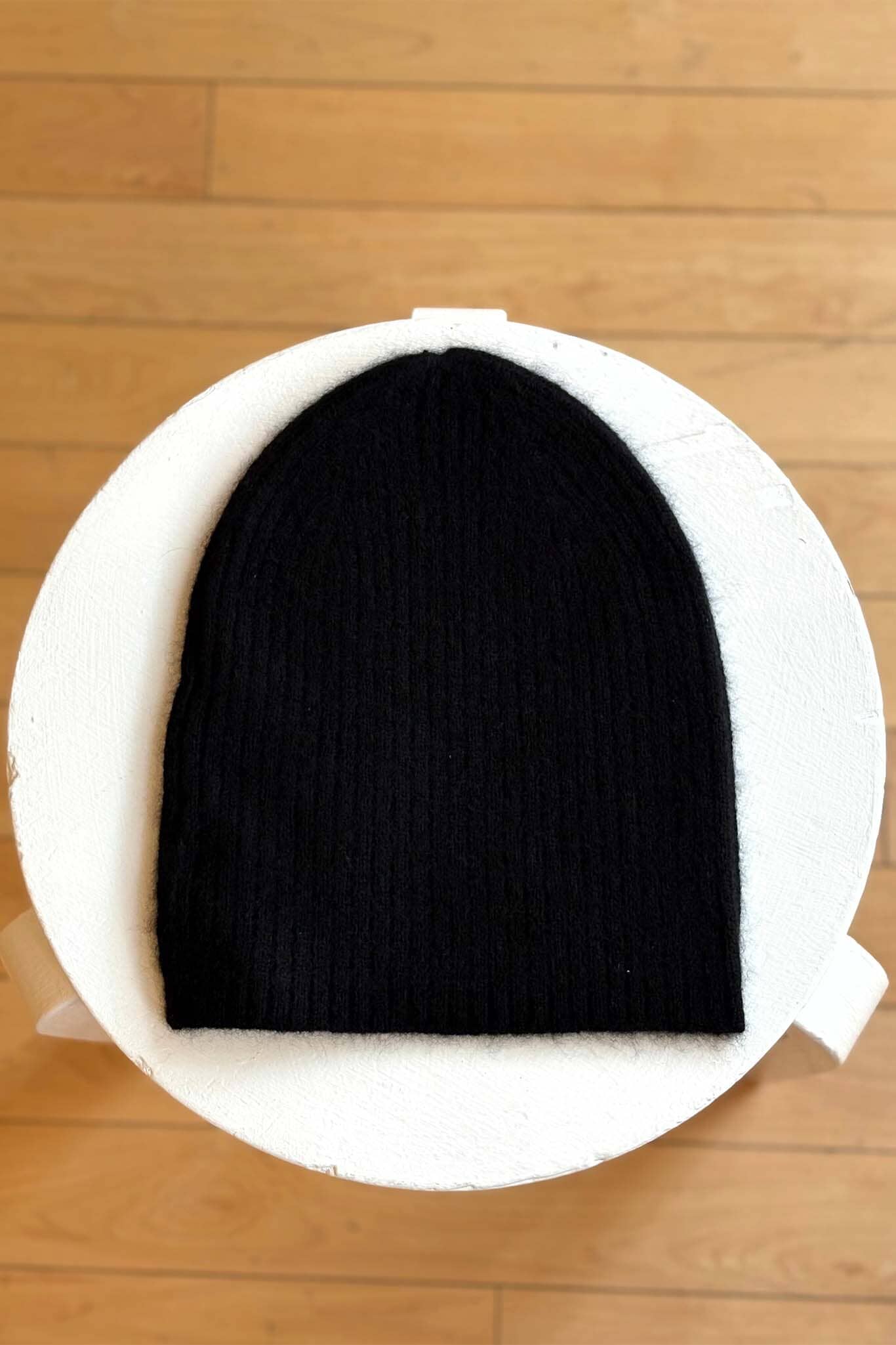 Black beanie on a white circular cushion with a wooden floor background