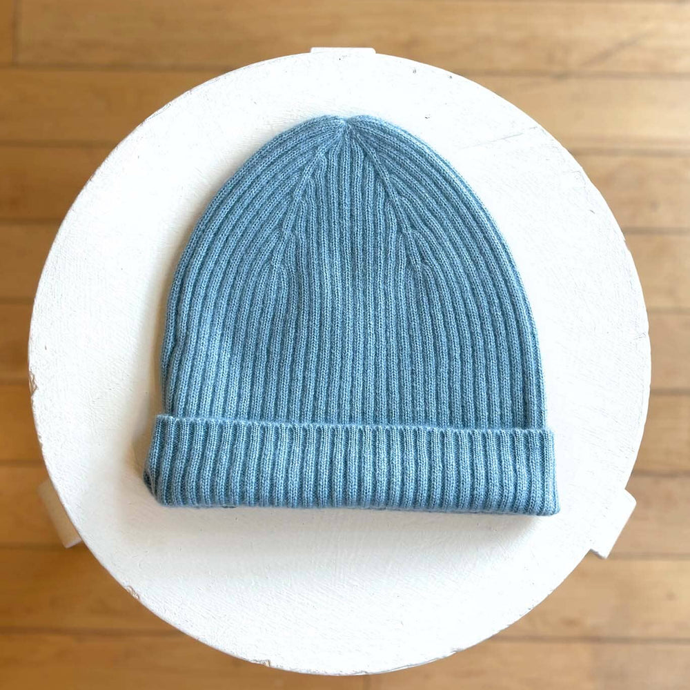 Sky blue knit beanie on a white circular platform with a wooden floor background