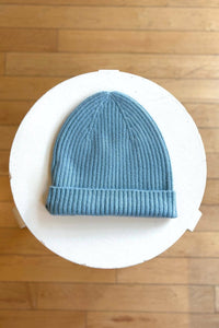 Sky blue knit beanie on a white circular platform with a wooden floor background