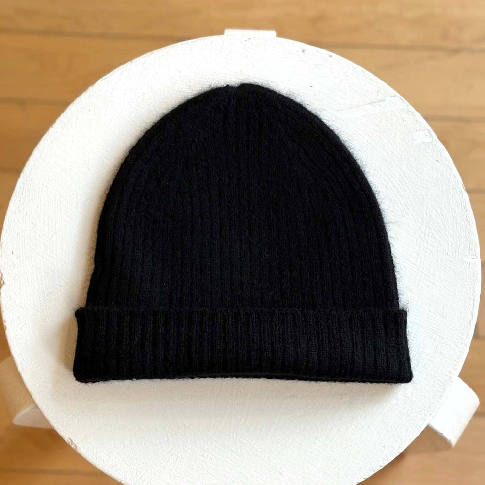 Black knit beanie on a white circular cushion with a wooden floor background