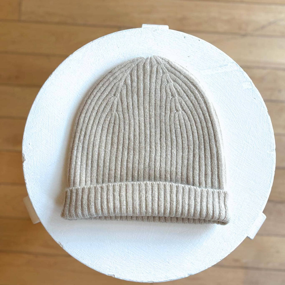 Beige knit beanie on a white circular stand against a wooden floor background