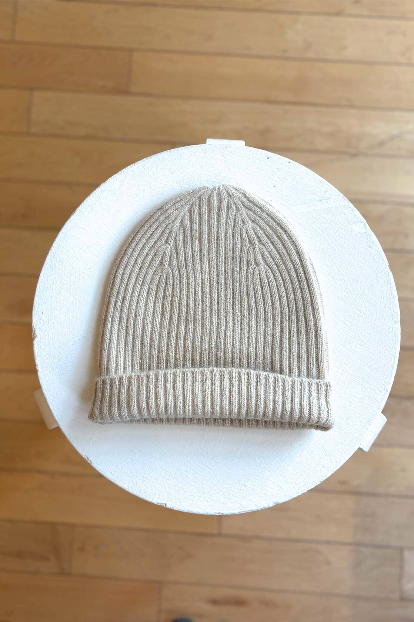 Beige knit beanie on a white circular stand against a wooden floor background