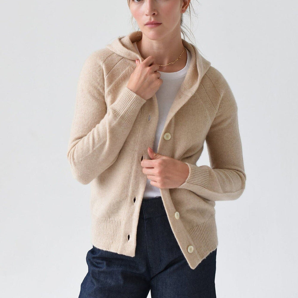 A woman wearing a beige cashmere hoodie with mother of pearl buttons and ribbed trims, paired with a white top and blue jeans