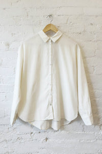 White long sleeve shirt on a wooden hanger against a white brick wall