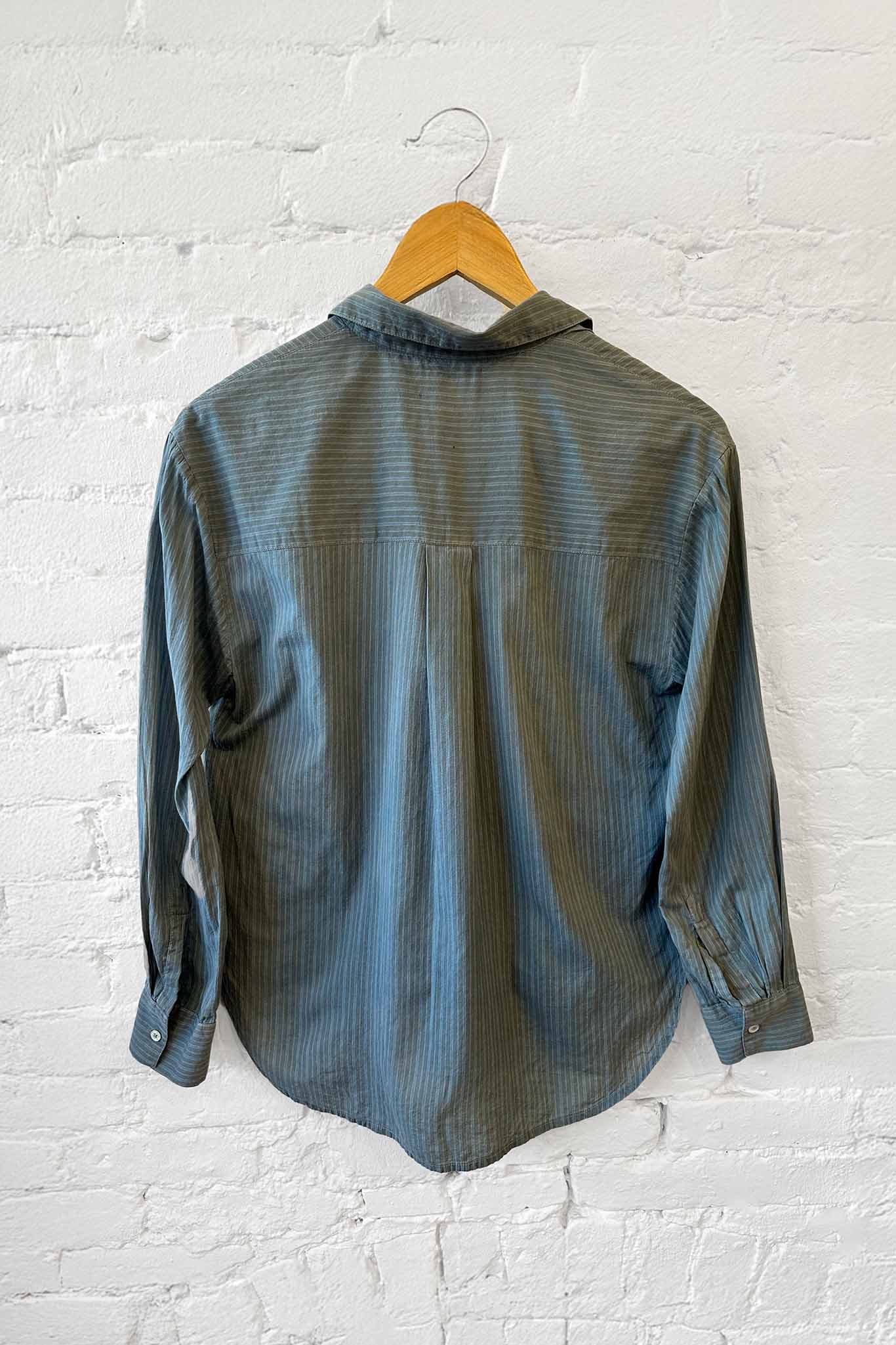 Green mineral long sleeve shirt on a wooden hanger against a white brick wall