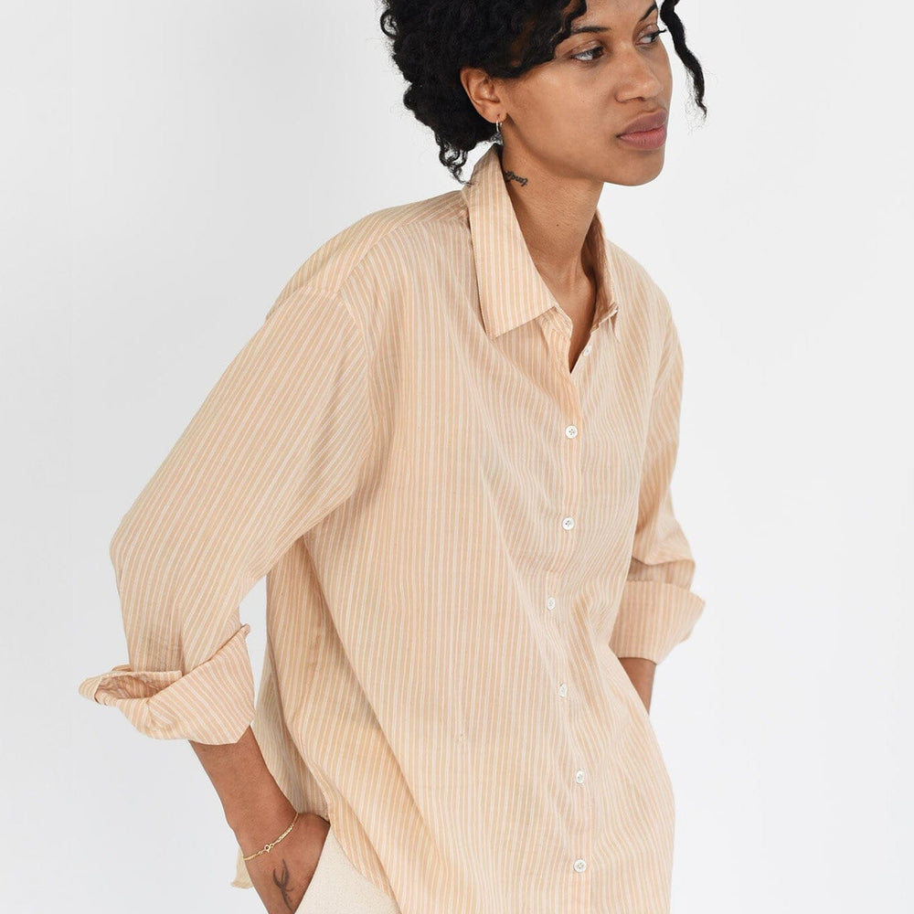 
                  
                    A woman wears a tan, golden striped long sleeve button down blouse. The top is lightweight and made of cotton. Available to purchase at M.Patmos in Brooklyn, New York. 
                  
                