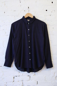 A dark navy blue long-sleeve button-up shirt hanging on a wooden hanger against a white painted brick wall.
