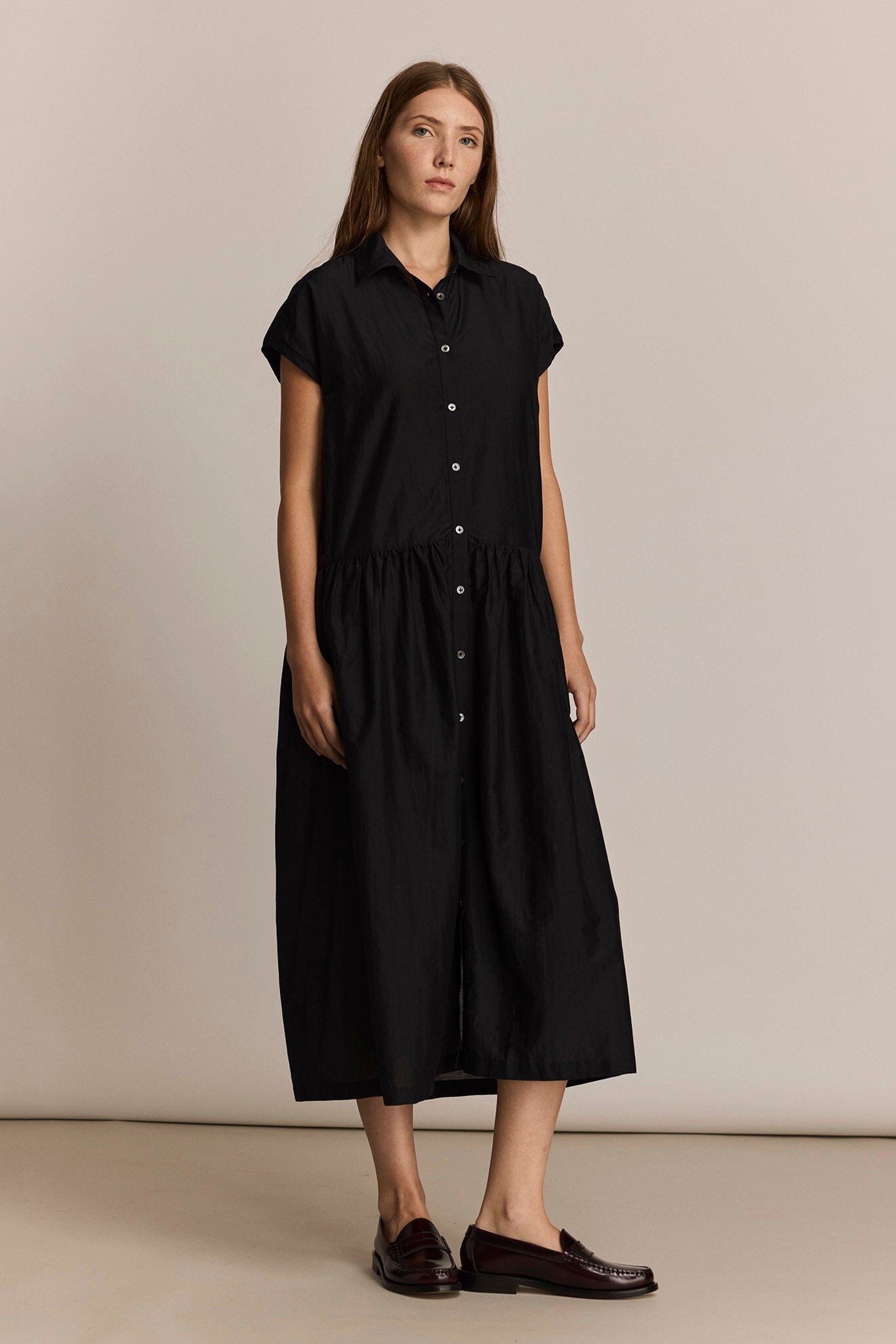 Woman wearing a black midi dress against a beige background